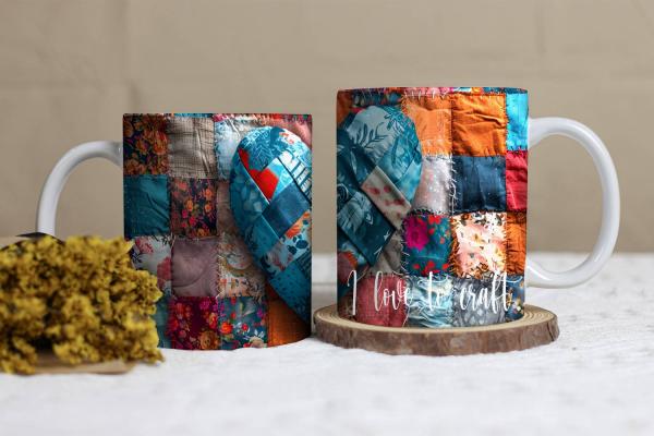 Weißer Keramikbecher mit einem Patchwork-Design in Form eines Herzens. Der Hintergrund besteht aus verschiedenfarbigen Stoffstücken in Blau-, Rot- und Orangetönen. Auf dem Becher steht in einer geschwungenen weißen Schrift: 'I love to craft'. Der Becher l